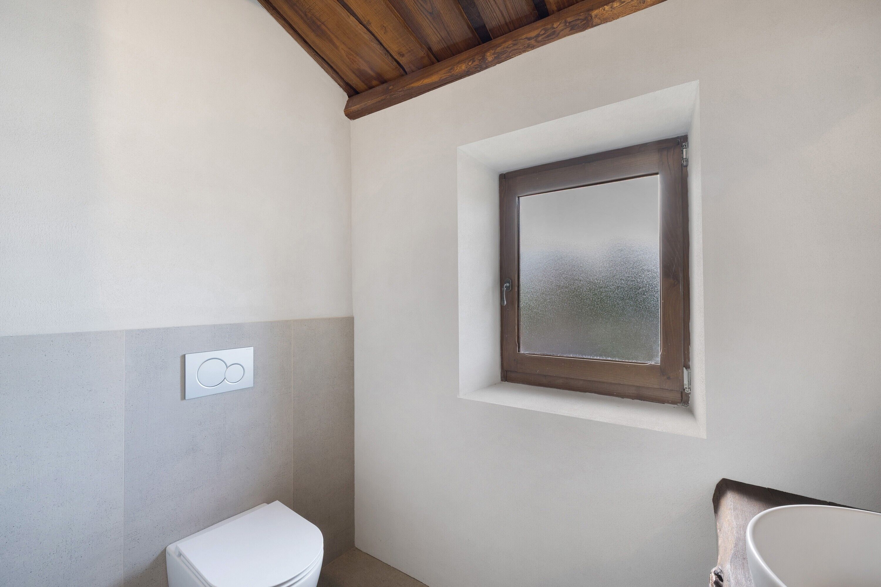 A bathroom with a toilet, a window, and a wall-mounted light switch.