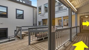 Une terrasse en bois avec une rambarde, une enseigne indiquant un bar à vin et un panneau d’avertissement signalant un sol glissant.