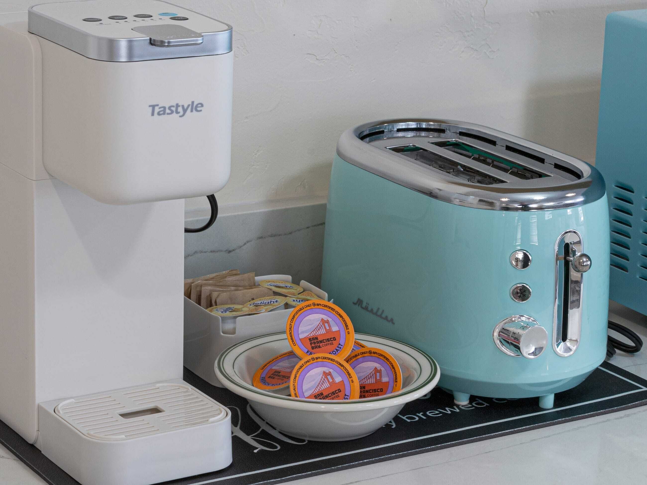 A coffee maker, a toaster, and a bowl with coffee pods on a kitchen counter.
