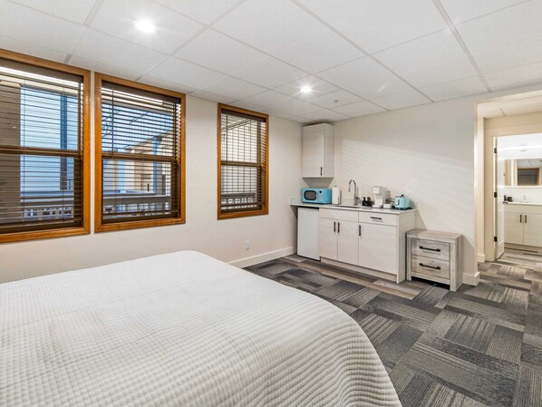 A bedroom with a bed, a kitchenette with a microwave, and a bathroom with a mirror.