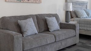 En grå sofa med mønstrede puder, en lampe og en seng med gråt sengegærde i et rum med et verdenskort på væggen.