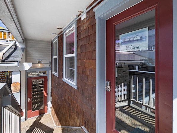 A residential property with a red door, a covered porch, and a view of a waterfront.