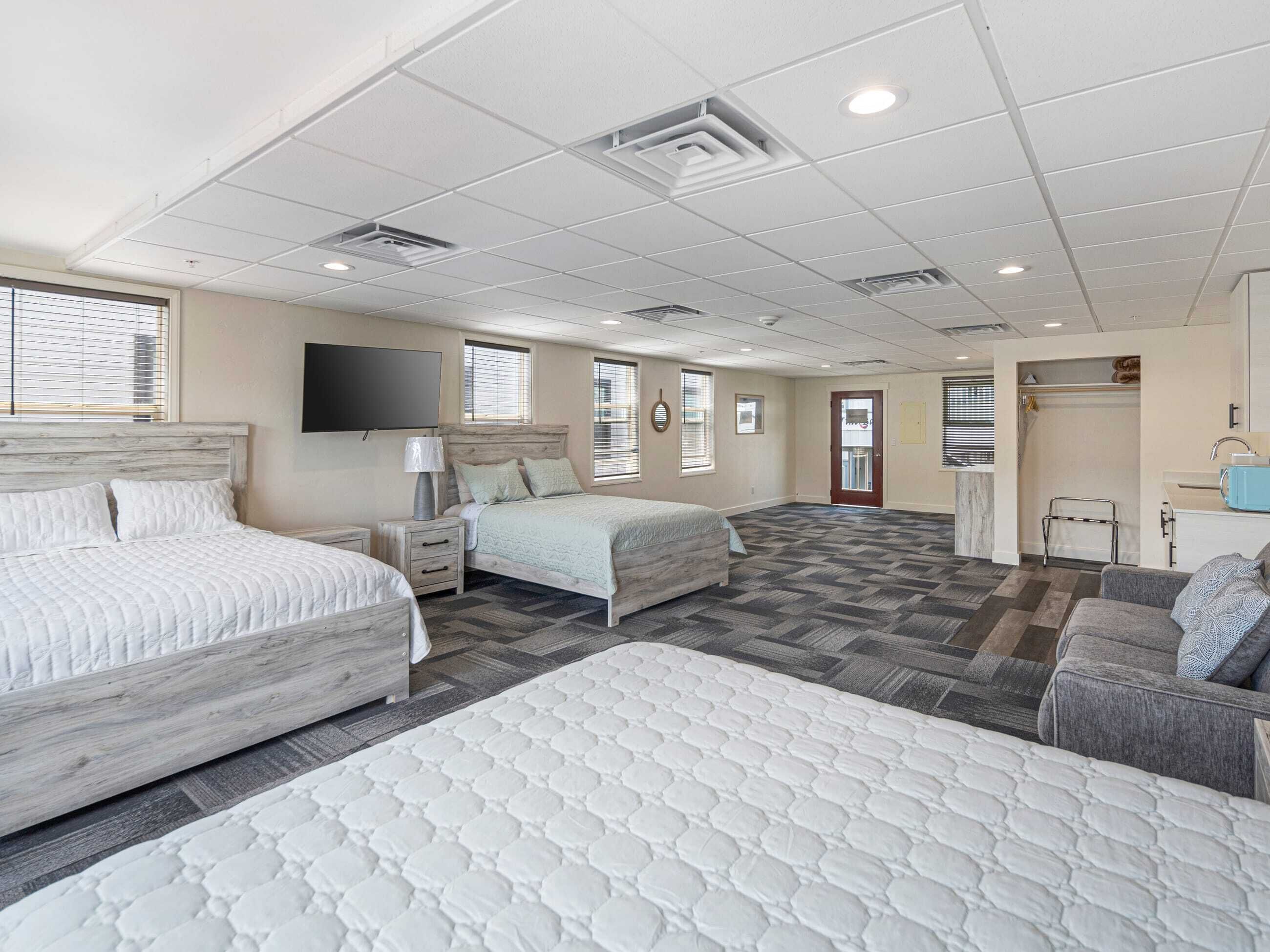 A hotel room with a large bed, a smaller bed, a sofa, a TV, and a bathroom with a shower.