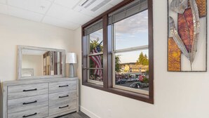 Une chambre d’hôtel avec une grande fenêtre, une commode, un miroir et une œuvre d’art accrochée au mur.