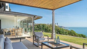 A modern outdoor living space with a glass wall, seating area, and a view of the sea. - Rbk Casa Concón remodel. vista increíble (Concon)