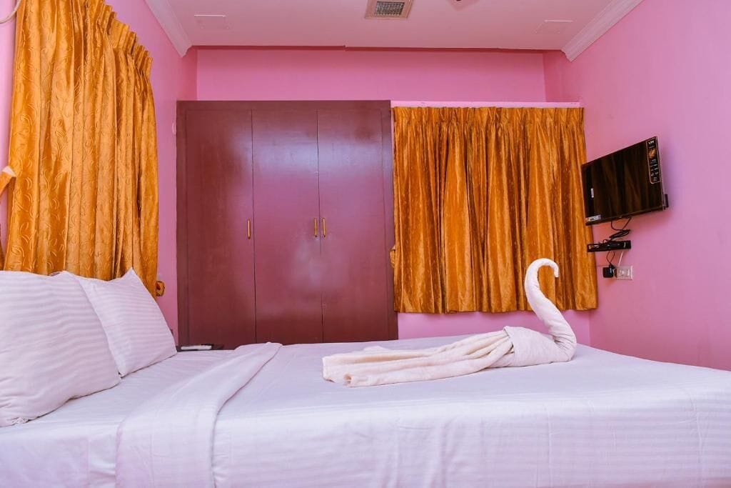 Una habitación de hotel con cama, armario, televisor y cortinas.