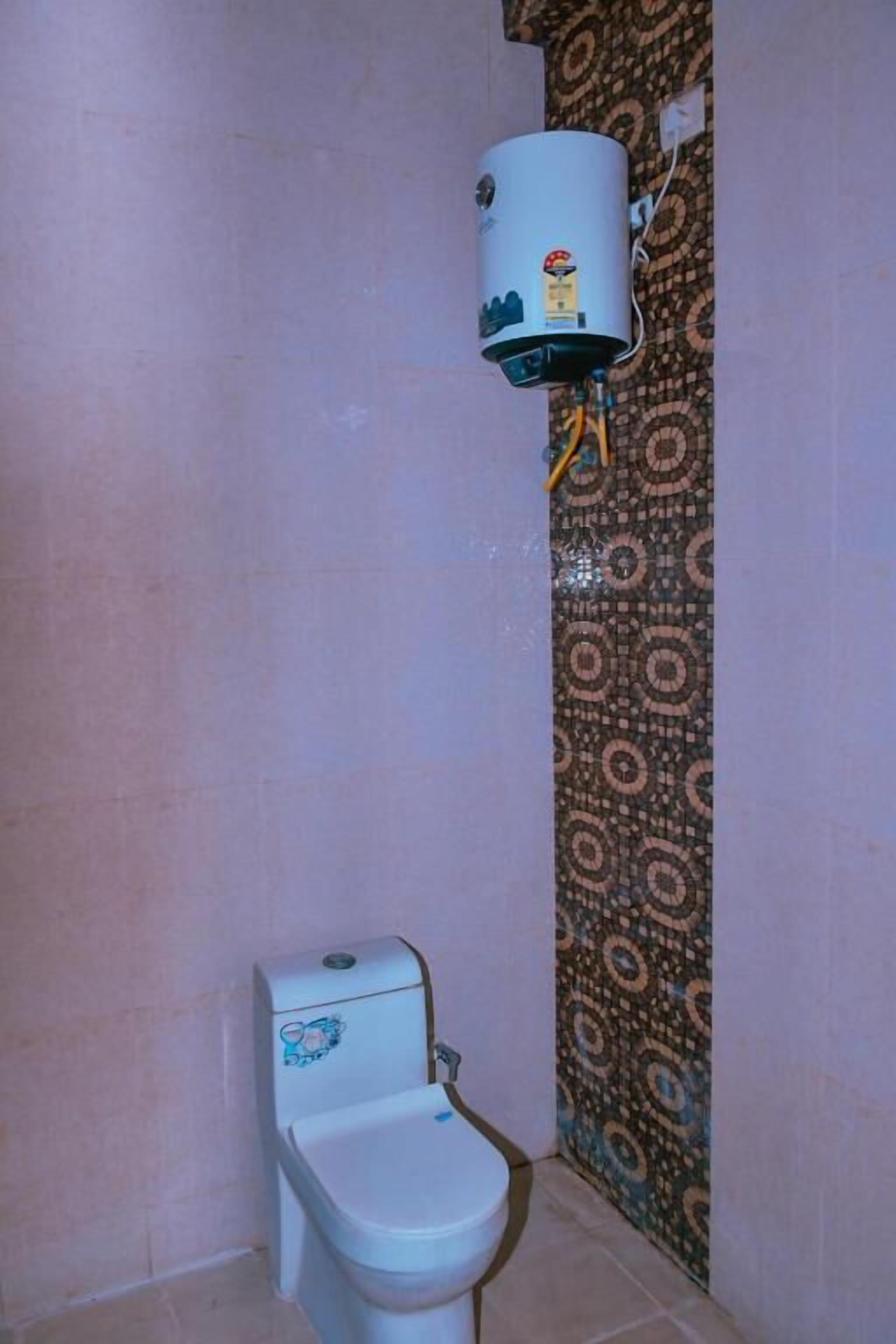 A bathroom with a toilet, a water heater, and patterned wallpaper.