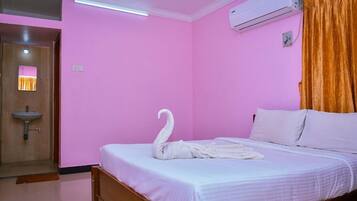 A bedroom with a bed, a white swan-shaped towel, an air conditioning unit, and a wooden door.
