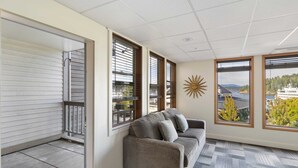 Una habitación con un sofá gris, ventanas amplias, un adorno de sol y vistas a un río y montañas.