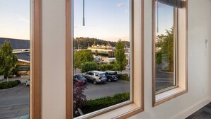 Habitación de hotel con ventanas amplias que dan a un estacionamiento y un edificio de enfrente.