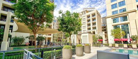 A modern outdoor pool area with a clear sky, surrounded by multi-story buildings with balconies.