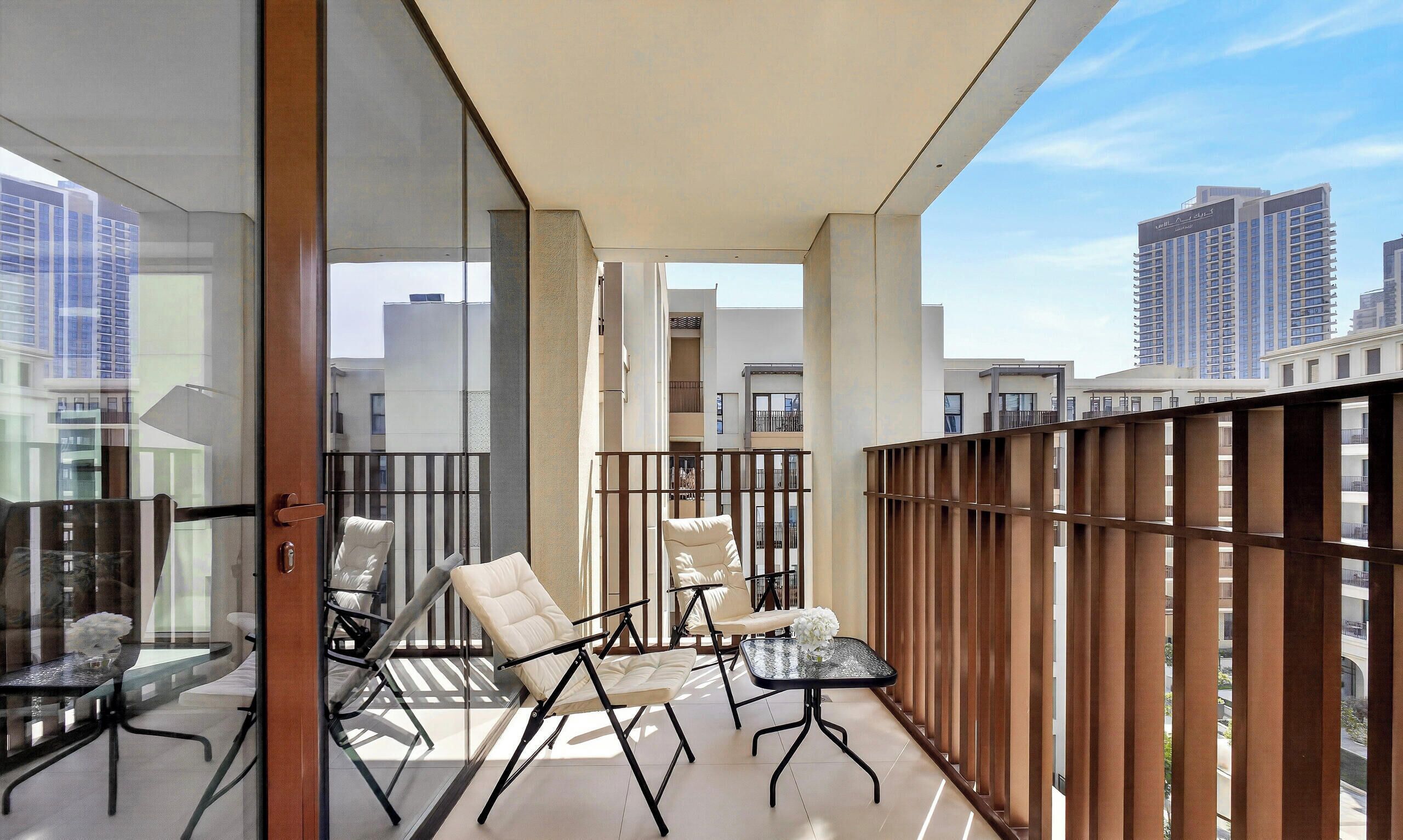 A balcony with modern furniture, glass walls, and a view of high-rise buildings.
