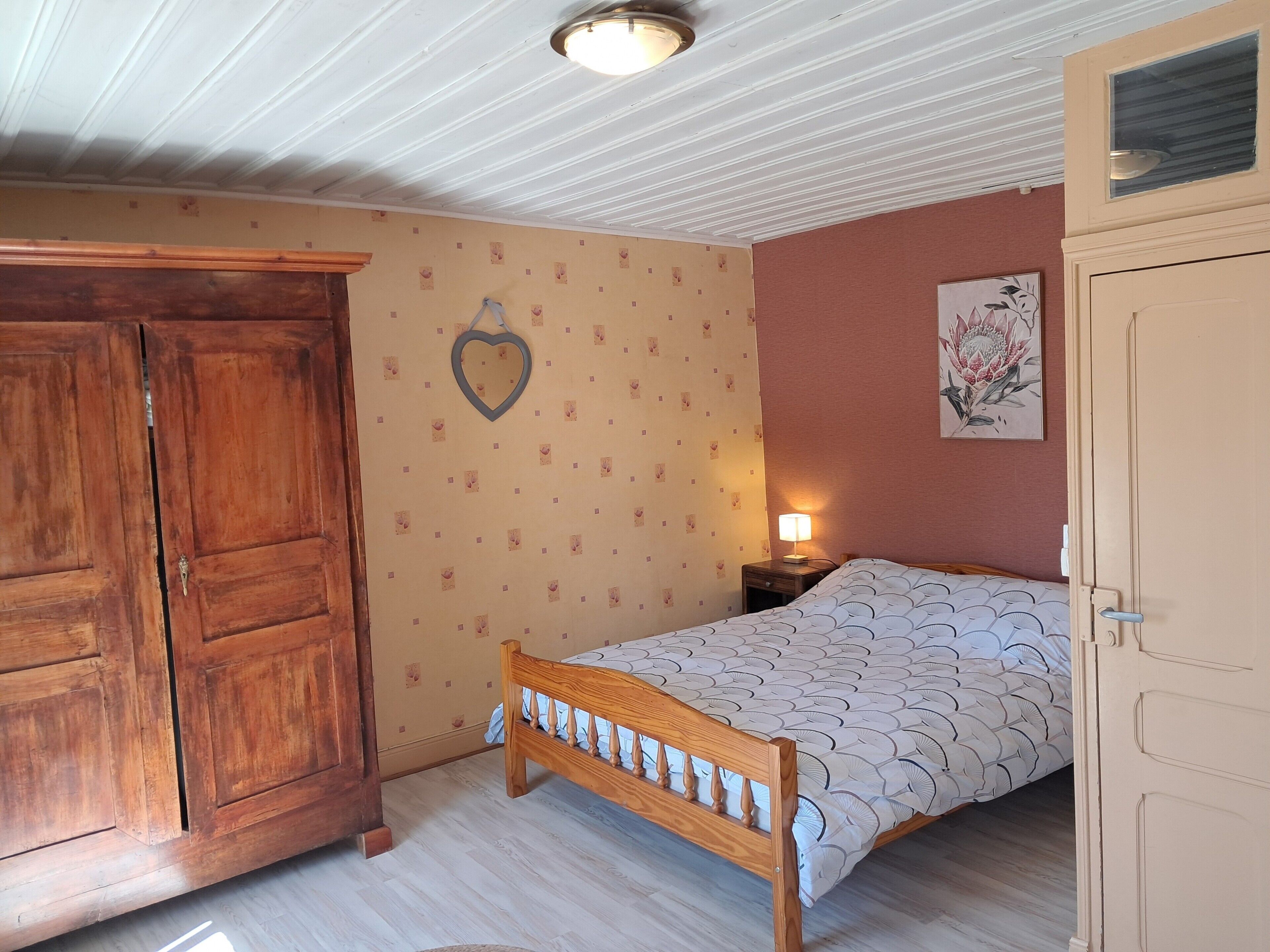 Een slaapkamer met een houten bed, een kledingkast, een nachtkastje met een lamp, en een muur met een decoratie in de vorm van een hart.