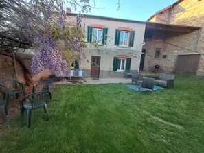 A house with a patio area, outdoor furniture, and a tree with purple flowers. - Holiday Home 'Gîte Les Glycines' (Auzon)