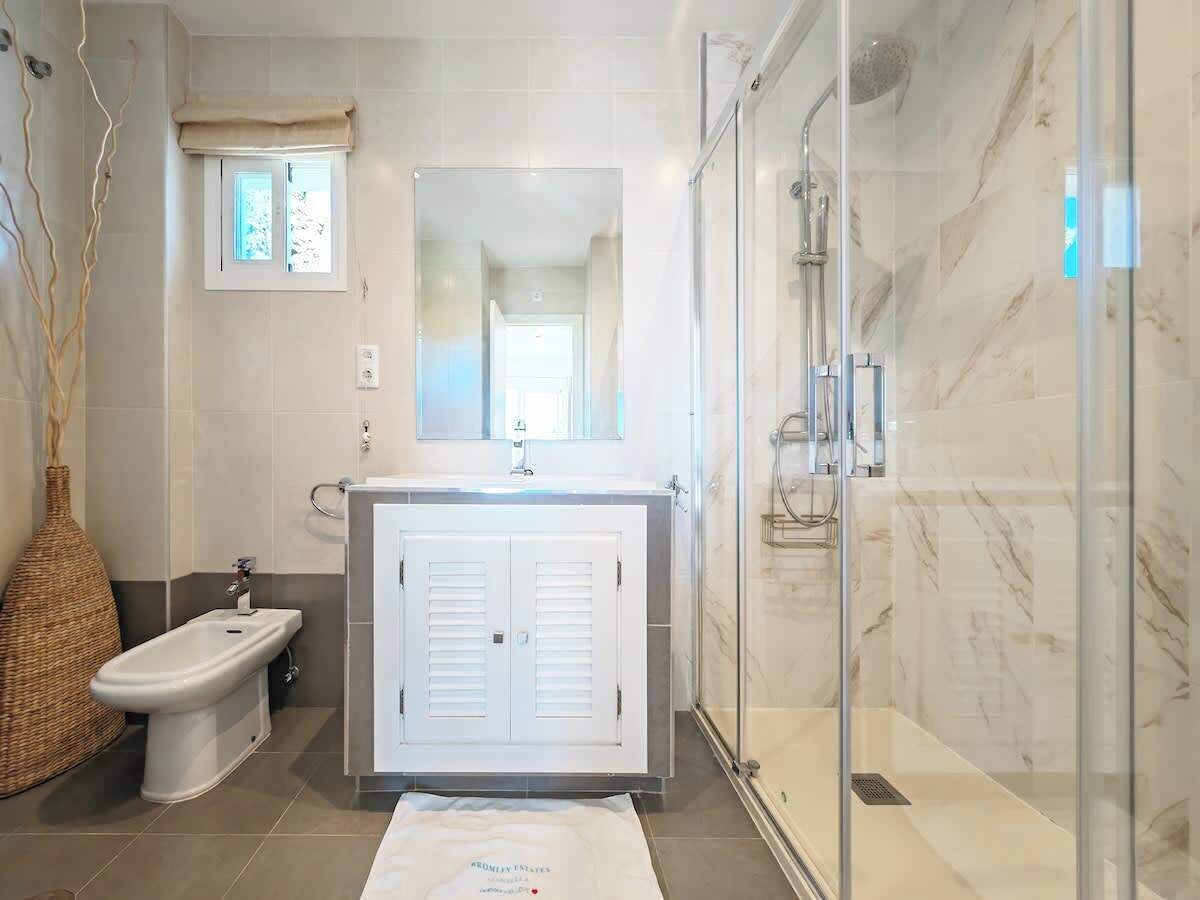 Un baño moderno con ducha envuelta en vidrio, un bidé, un lavabo con armarios y un espejo grande.