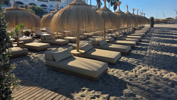 Een strandlounge met rieten parasols, comfortabele stoelen en een houten terras.