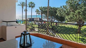Ein Balkon mit freiem Blick auf das Meer, Palmen und eine Rasenfläche.