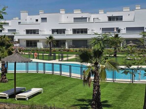 Un hotel moderno con piscina, tumbonas y césped cuidado.