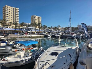 Un puerto deportivo con varias embarcaciones amarradas, cielo despejado y edificios al fondo.