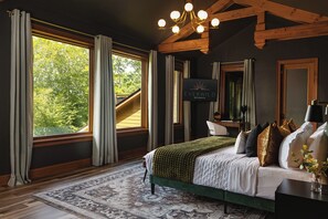 A bedroom with a large bed, a desk, a TV, and a view of the outdoors.