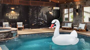 Une piscine intérieure avec un flotteur en forme de cygne, des chaises longues en bois et une fresque murale portant l’inscription « THE CANOPY CLUB ».