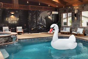 An indoor swimming pool with a swan float, wooden deck chairs, and a mural with the text 'THE CANOPY CLUB'.