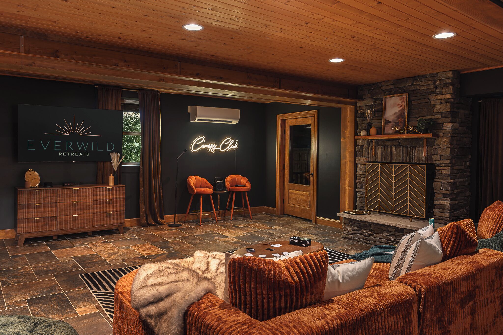 Un'accogliente area relax con camino, un neon e una televisione che mostra 'Everwild Retreats'.