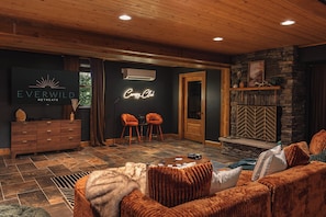 A cozy lounge area with a fireplace, a neon sign, and a television displaying 'Everwild Retreats.'