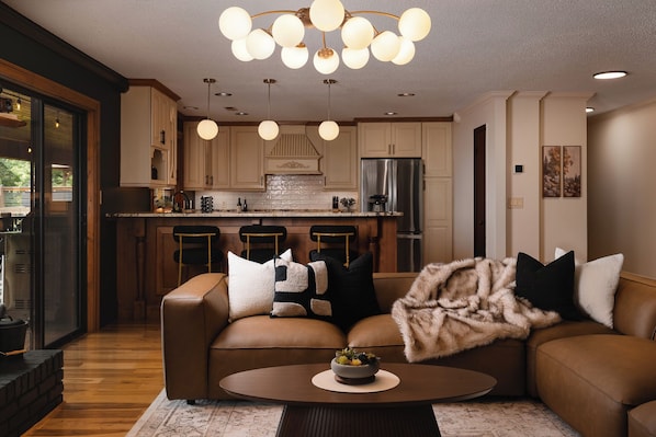 A modern living room with a brown leather sofa, a coffee table with a bowl, and a fireplace with a fur throw.