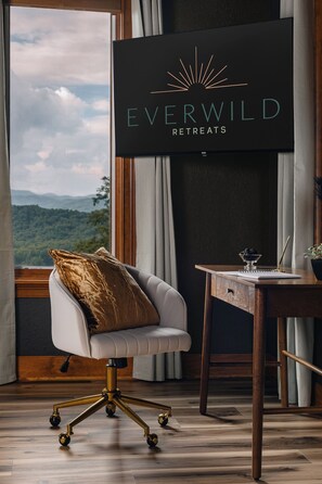 A modern room with a view of the mountains, a comfortable chair, a desk with a notebook and pen, and a sign for Everwild Retreats. - Indoor Pool Resort • Hot Tub + Sauna • Rooftop • Speakeasy • Caboose (Pisgah Forest)
