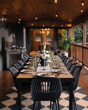 A long dining table set for a meal with chairs, candles, and a view of the outdoors.