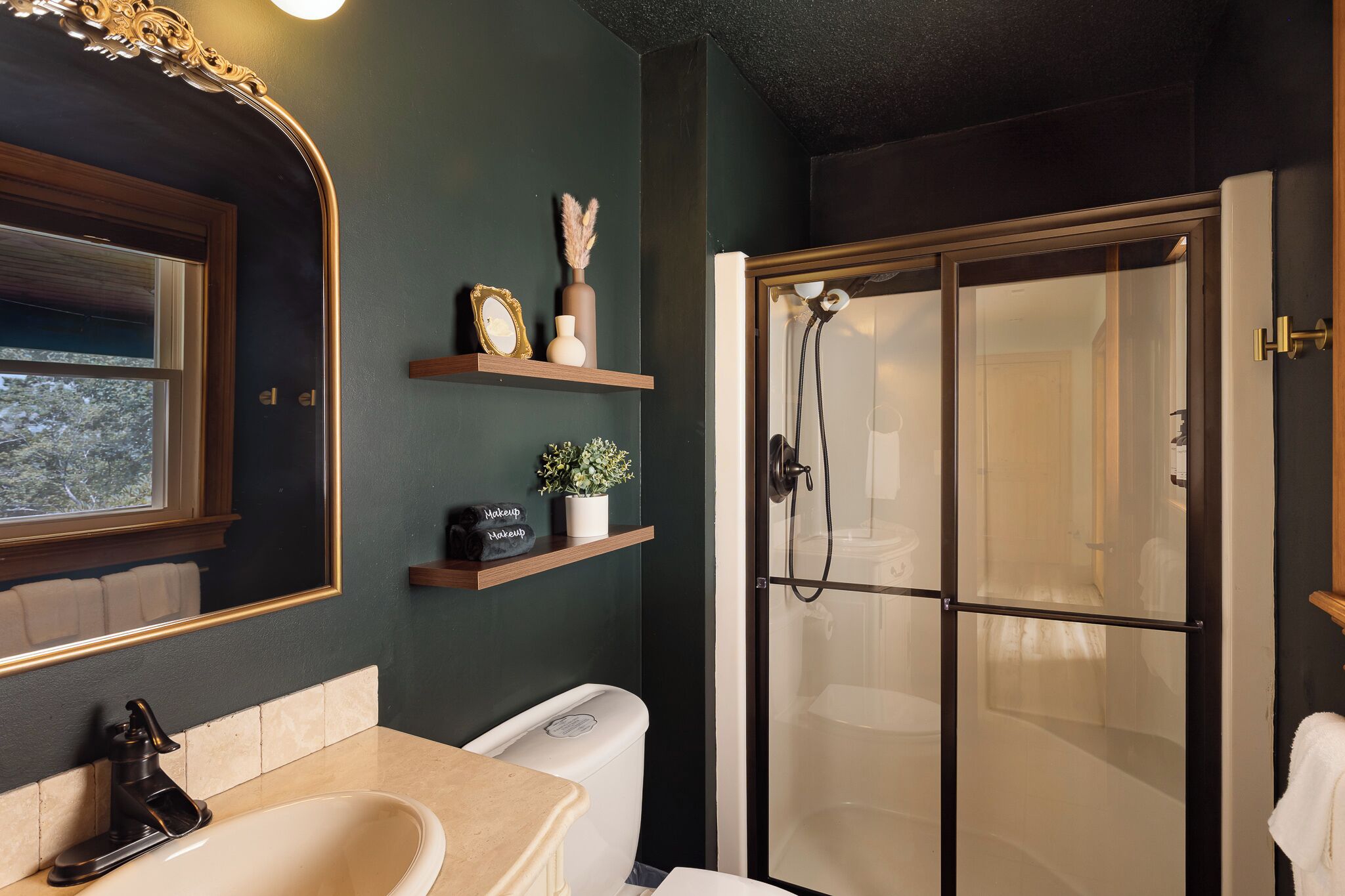 Ein Badezimmer mit Dusche, Waschbecken und Spiegel. Regale mit Dekorationselementen und eine Toilette sind ebenfalls vorhanden.
