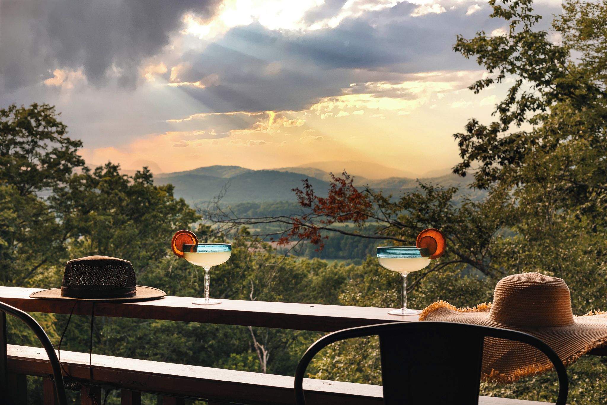 Ein Tisch mit zwei Getränken und einem Hut, mit Blick auf eine gebirgige Landschaft.