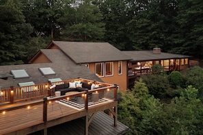 A two-story house with a deck, a fireplace, and a large window overlooking a forest.