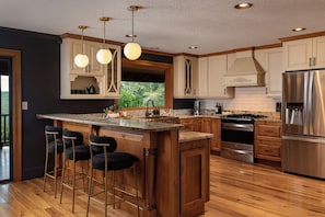 A modern kitchen with a central island, bar stools, stainless steel appliances, and wooden cabinetry.