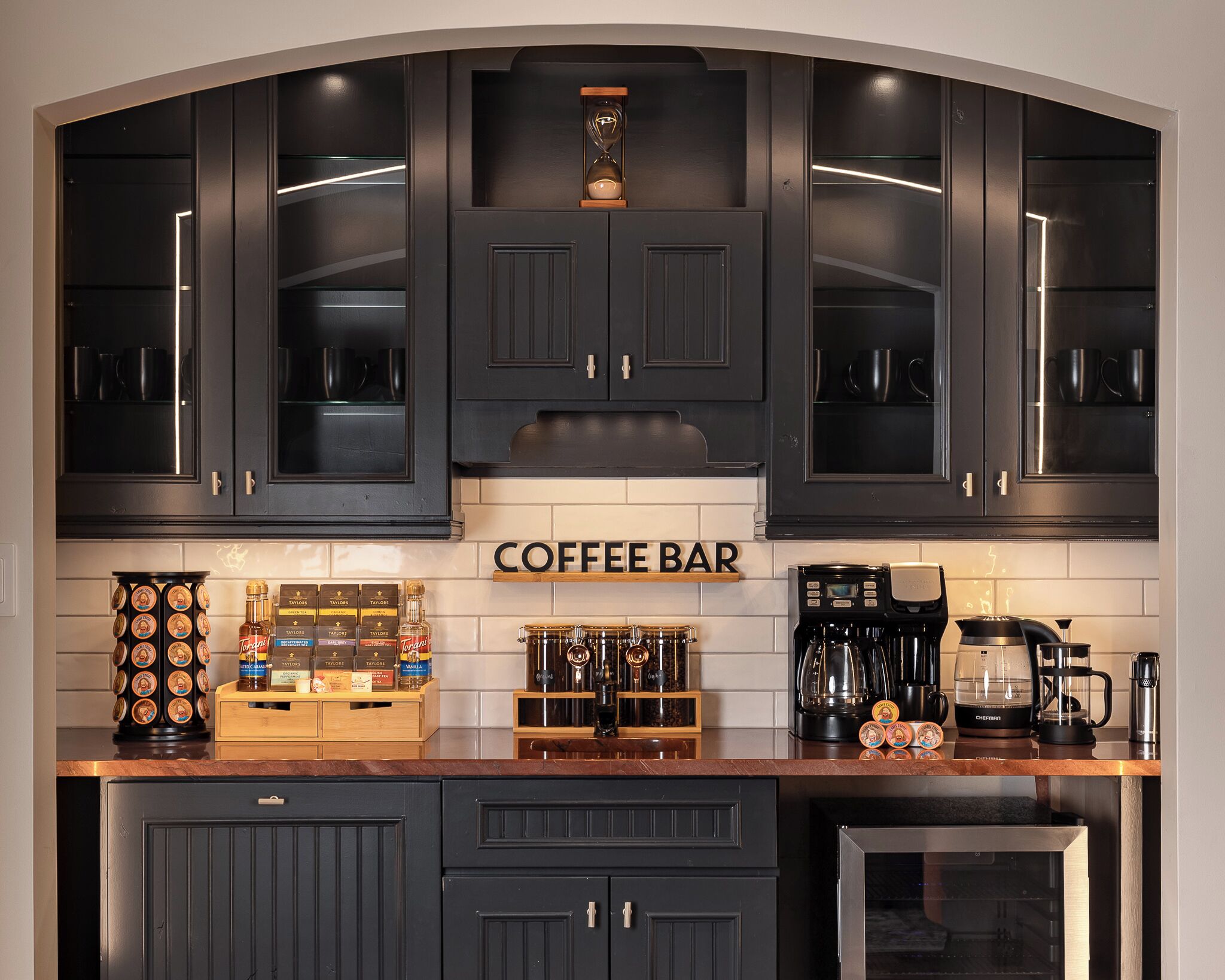 Eine Küche mit dunklen Schränken, einer Kaffeebar und diversen Kaffeemaschinen.