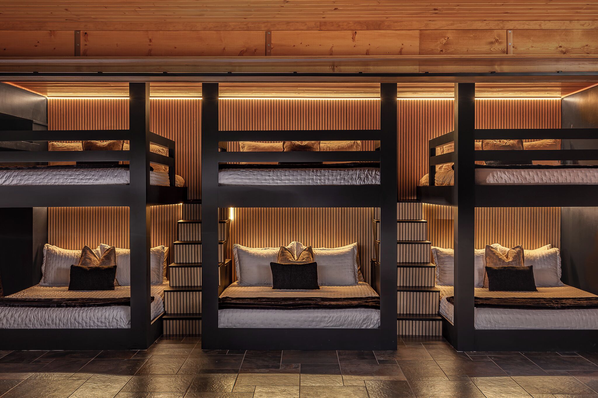 A multi-level bunk bed room with built-in lighting and a wooden ceiling.
