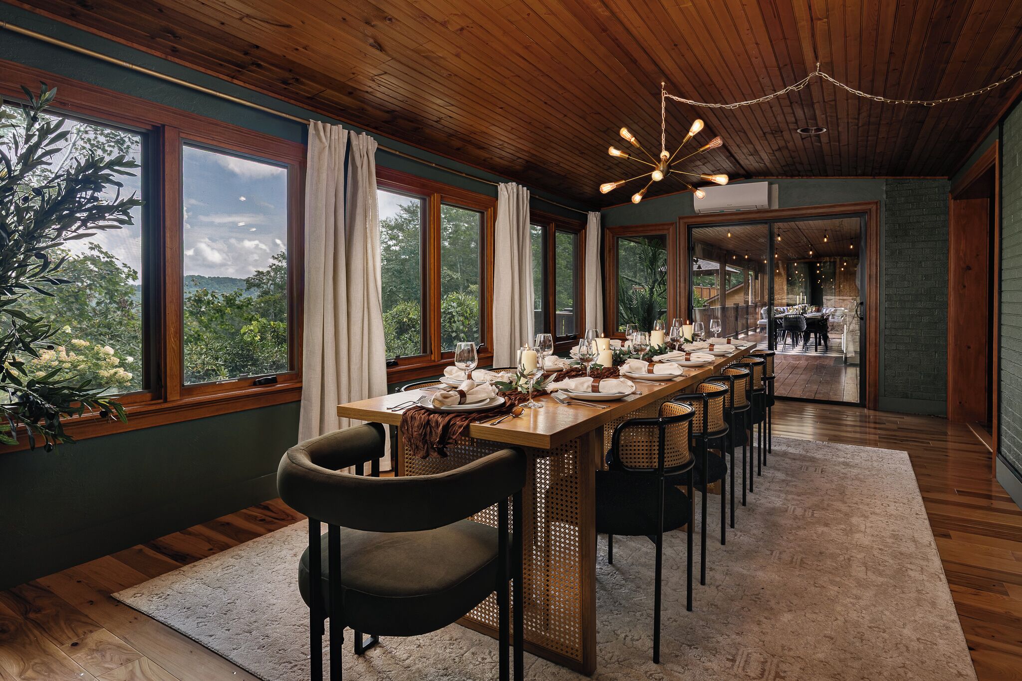 Un comedor con una larga mesa lista para una comida, rodeada de sillas, y vistas a zonas verdes al exterior.