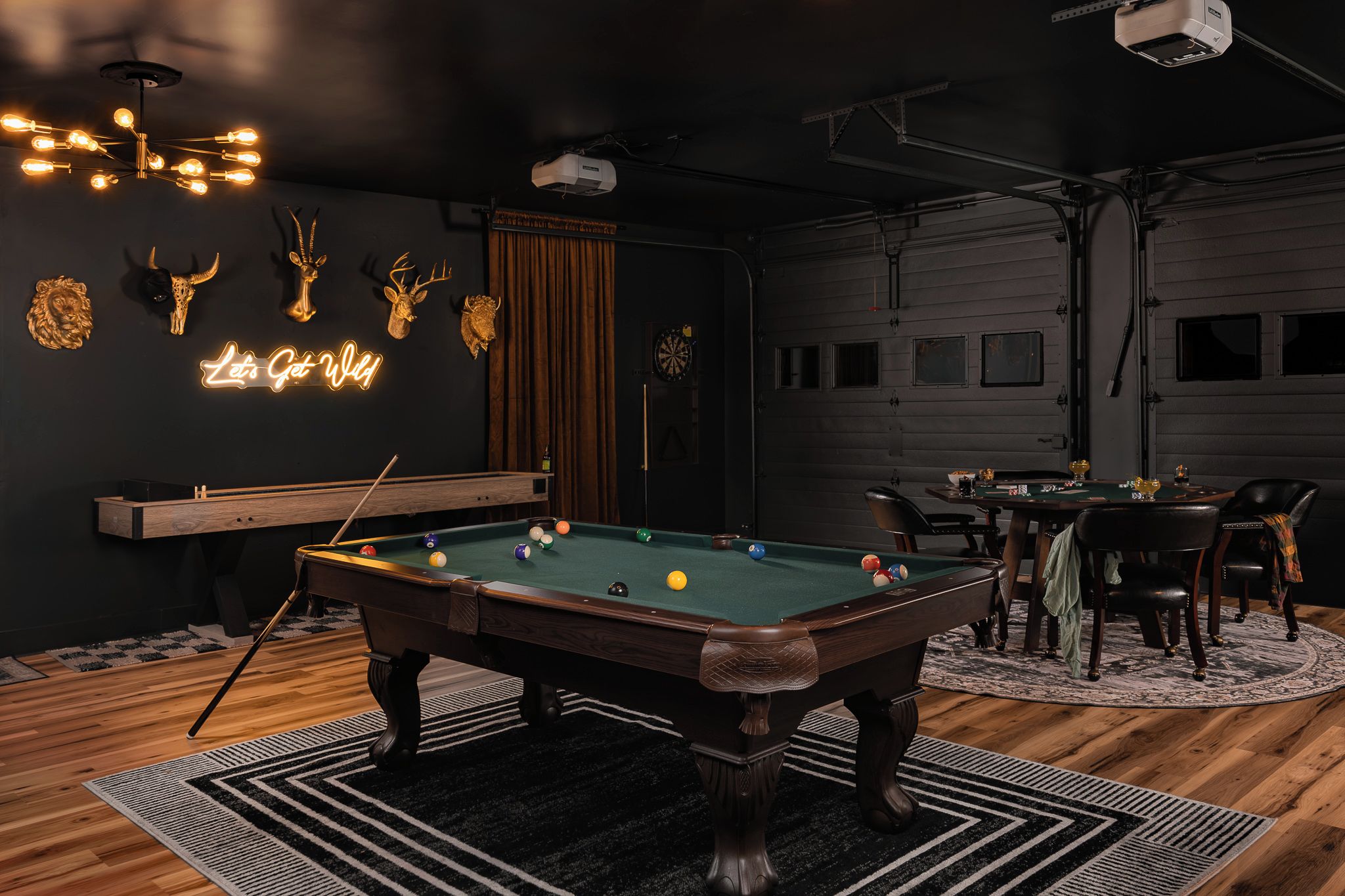 Une table de billard dans une pièce ornée d’un néon, de trophées et d’un jeu de fléchettes.