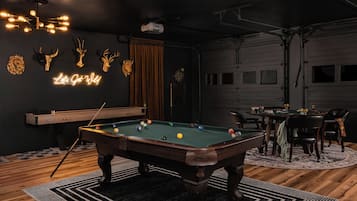 A pool table in a room with a neon sign, trophies, and a dartboard.