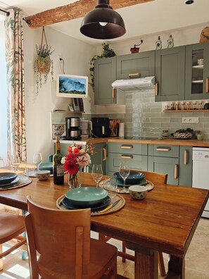 A kitchen with a dining table set for two, a hanging plant, and a television mounted on the wall. - Between the vineyards and the canal. Fully renovated 3-story house (Azille)