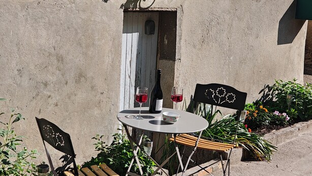 En terrasse med et bord, stole og en flaske vin.