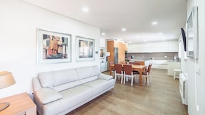 Una sala de estar moderna con un sofá, una mesa de comedor y sillas, una cocina al fondo y una obra de arte en la pared.