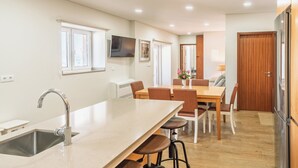 Una cocina moderna con una isla grande, un comedor con sillas, una puerta de madera y un televisor de pantalla plana montado en la pared.