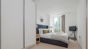 Ett modernt hotellrum med en stor säng, en tv på ett stativ, ett nattduksbord med en lampa och ett fönster med utsikt över staden.