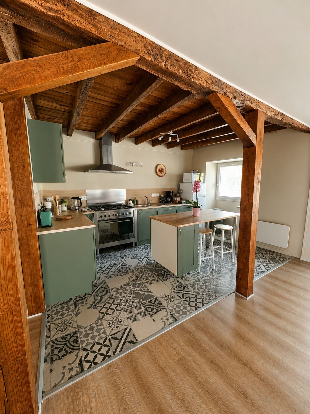 A kitchen with wooden beams, green cabinets, a tiled floor, and a window.