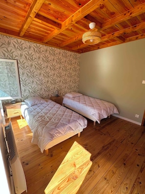 Una habitación con dos camas, suelo de madera, papel tapiz estampado y un ventilador de techo.