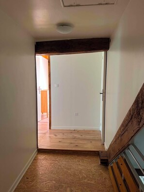 Un pasillo con suelo de madera, una puerta blanca al fondo y una escalera de madera a la derecha.