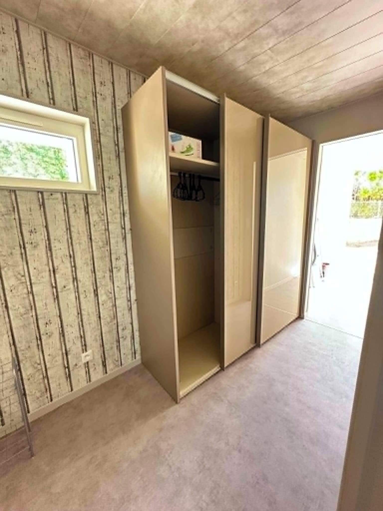 Ein Zimmer mit einer Holzwand, einem gerahmten Bild und einem Kleiderschrank mit geöffneten Türen.