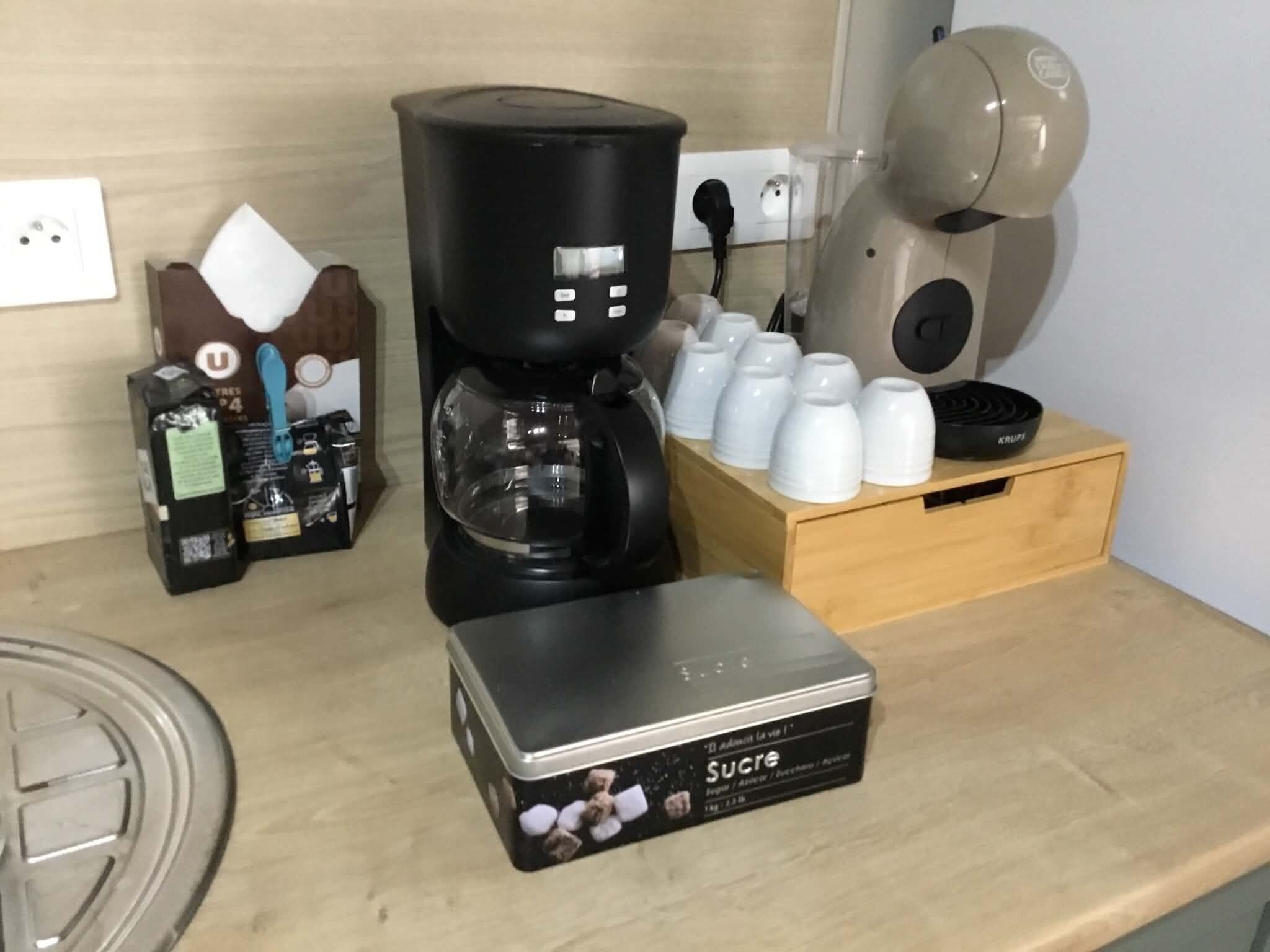 A kitchen area with a coffee maker, a box of sugar, and a set of white cups on a wooden counter.